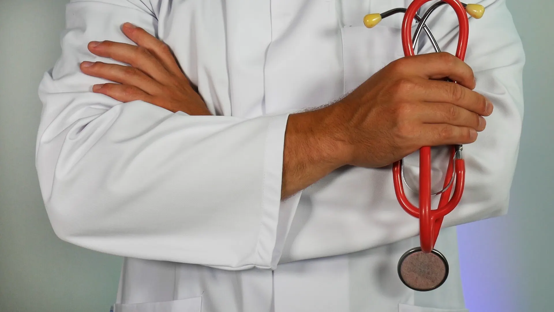 A doctor in a white lab coat with arms crossed, holding a red stethoscope.