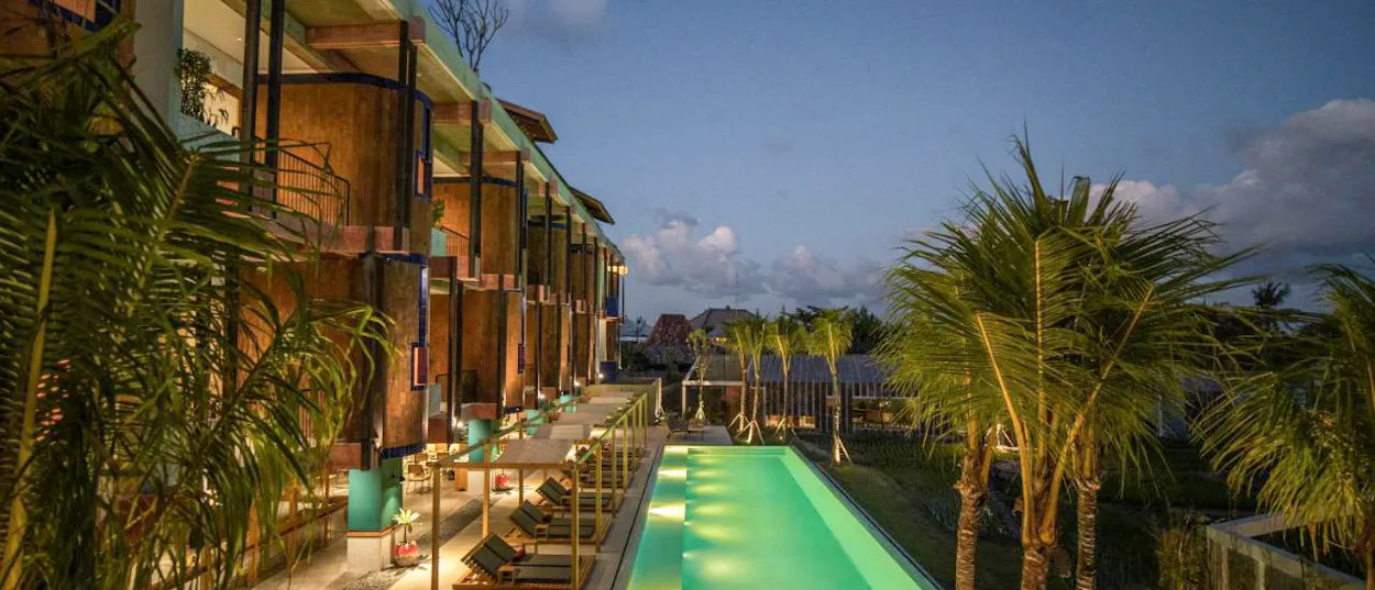 A luxurious resort in Canggu, Bali, with a long illuminated swimming pool and palm trees at dusk.