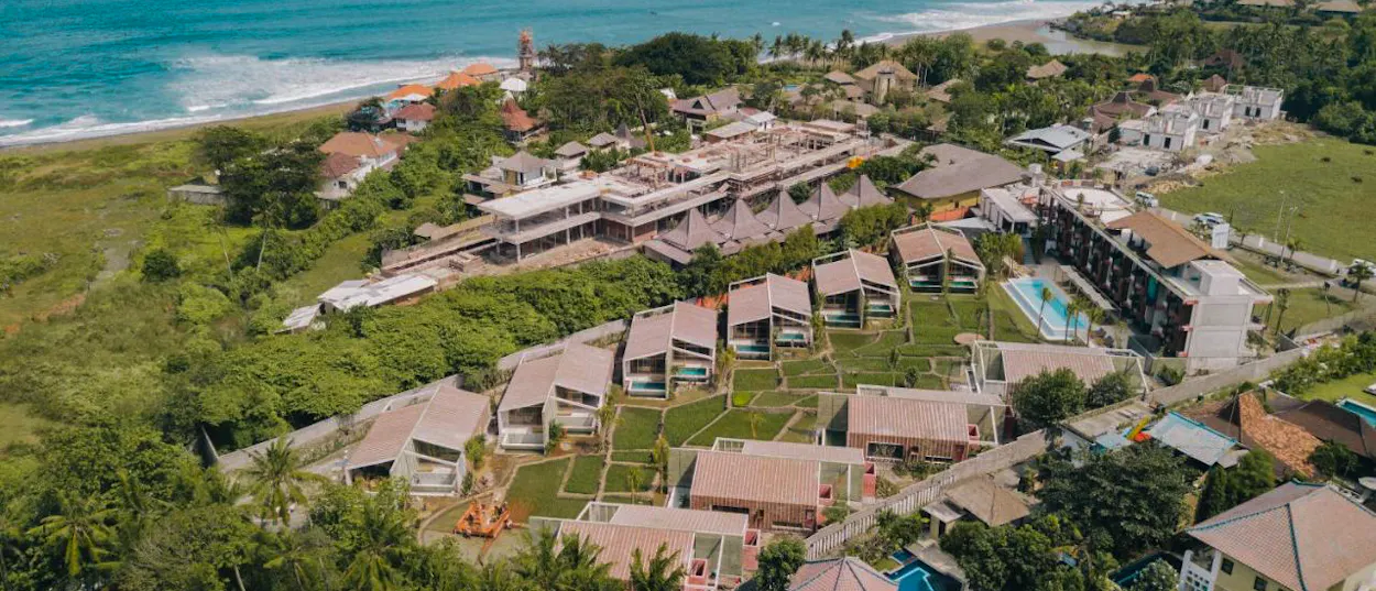 Aerial view of a modern resort complex with villas and pools along the scenic Canggu coastline.