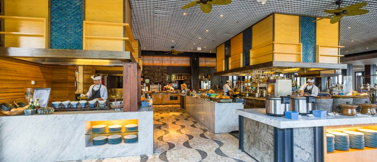 A bright, modern hotel restaurant in Kuta, Bali, with chefs preparing food at buffet stations.