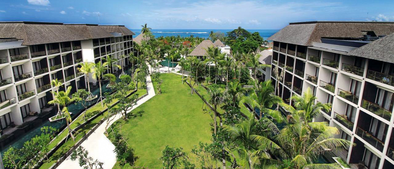A tropical resort in Kuta, Bali, with large buildings, lush gardens, and a view of the ocean.