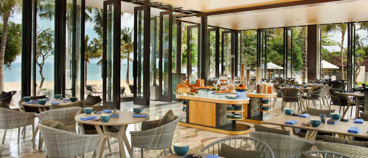 A modern resort restaurant in Kuta, Bali, featuring a breakfast buffet and open views to the beach.