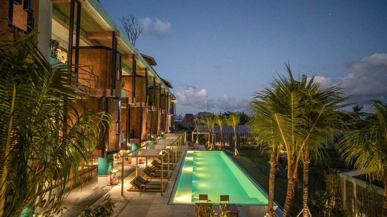 A luxurious resort pool illuminated at dusk, surrounded by palm trees and modern architecture in Bali.
