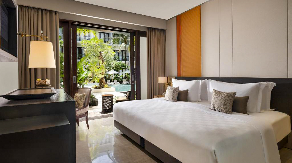 An elegant hotel bedroom in Bali with a large bed and direct access to a tropical pool.
