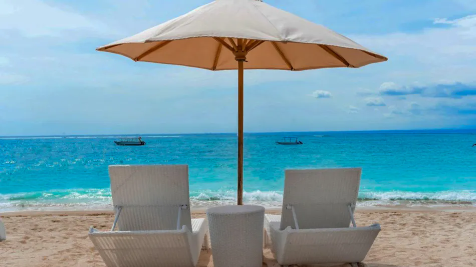 White lounge chairs and umbrella on a sandy beach overlooking the turquoise ocean at Nusa Lembongan.