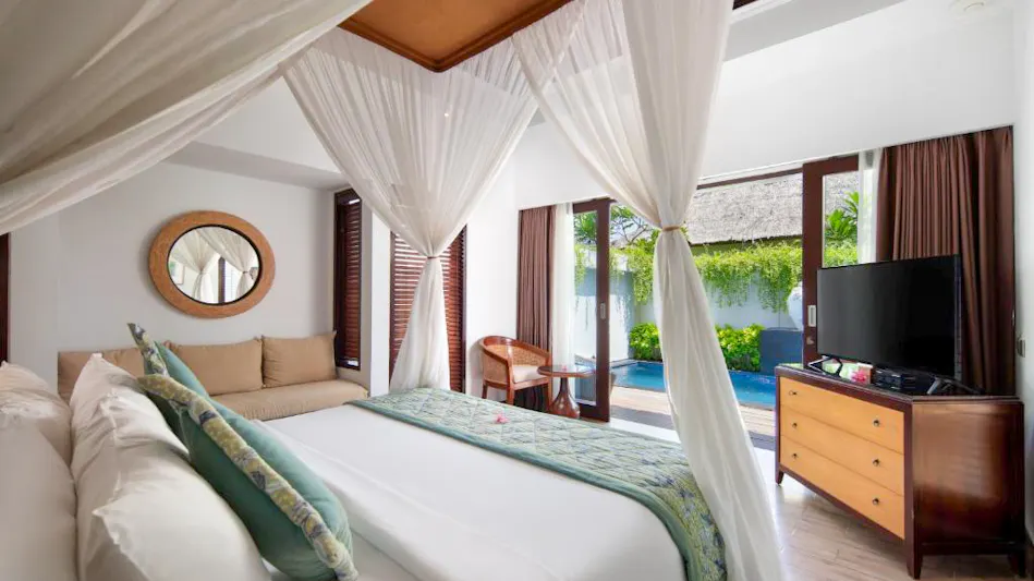 Luxurious resort bedroom with a four-poster bed and white netting, opening to a private pool.