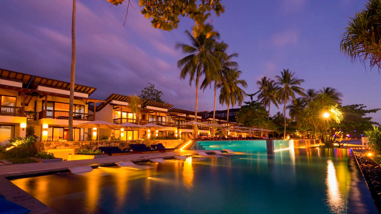 Luxury Katamaran Resort in Lombok at twilight, with warm lights illuminating buildings and a large pool.