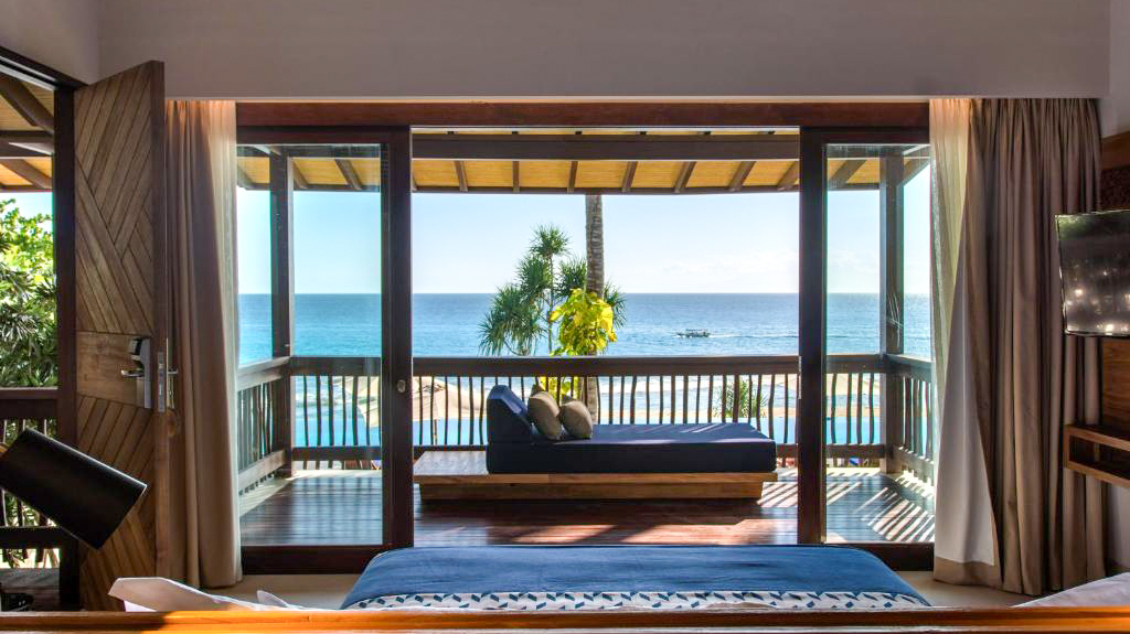 Luxurious resort room in Lombok with a balcony daybed overlooking the sparkling blue ocean.