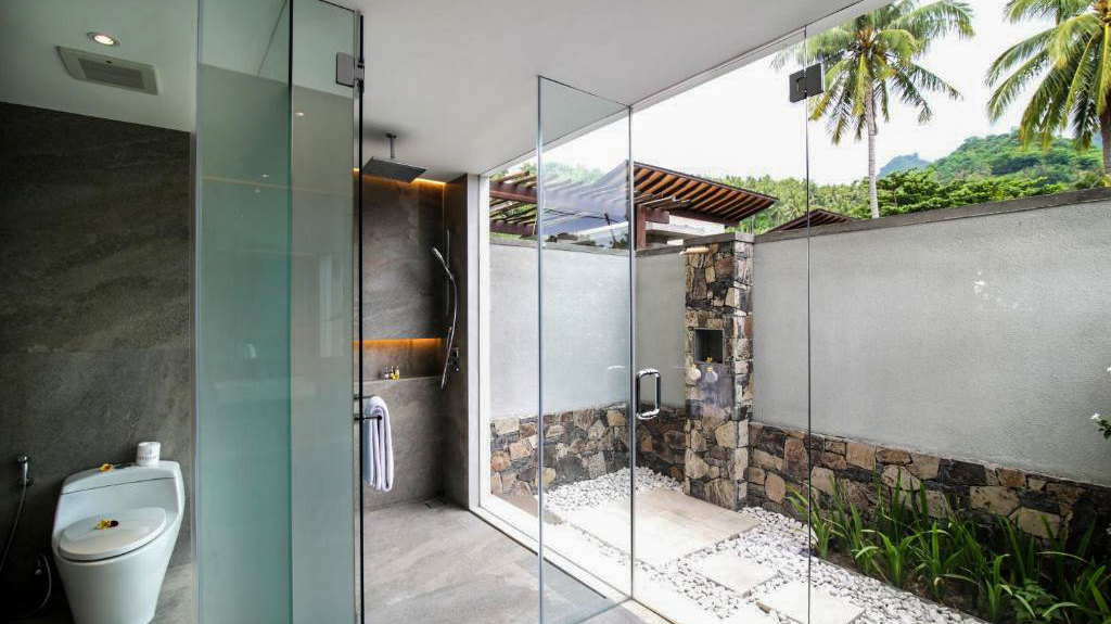 Modern glass shower and private outdoor garden with tropical plants and palm trees in Lombok.