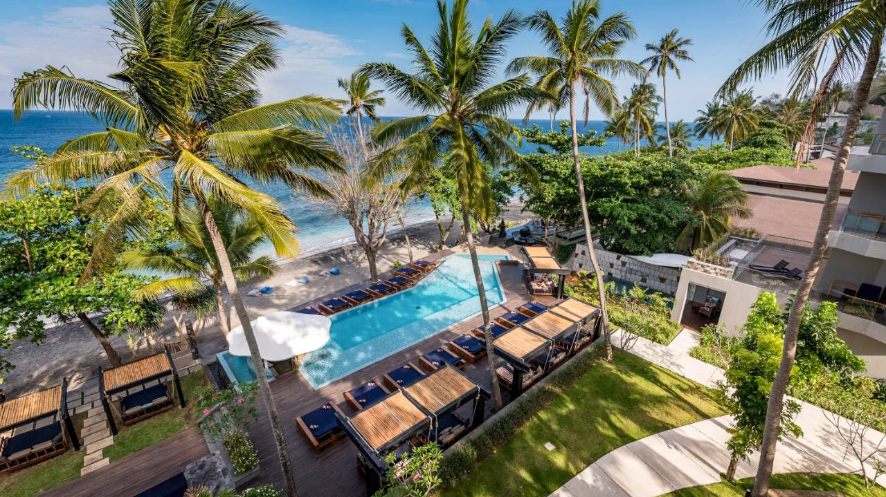 Luxurious Katamaran Resort in Lombok with a large swimming pool, lush palm trees, and ocean.