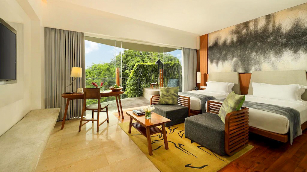 Luxurious hotel room with two beds, a comfortable seating area, and a balcony with tropical views.
