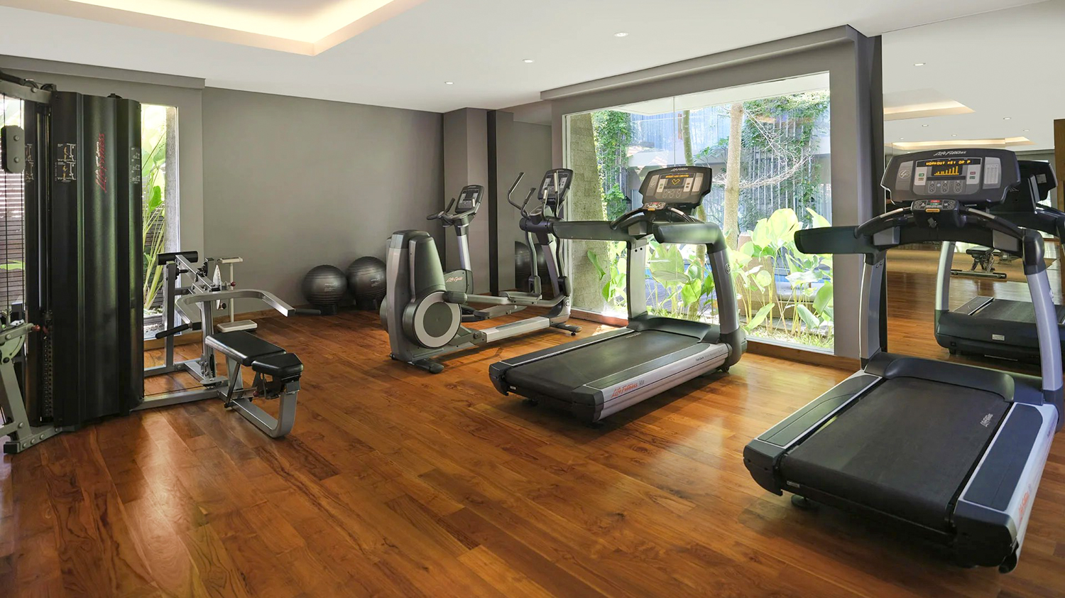 Bright and modern resort fitness center with various exercise machines and a view of lush gardens.