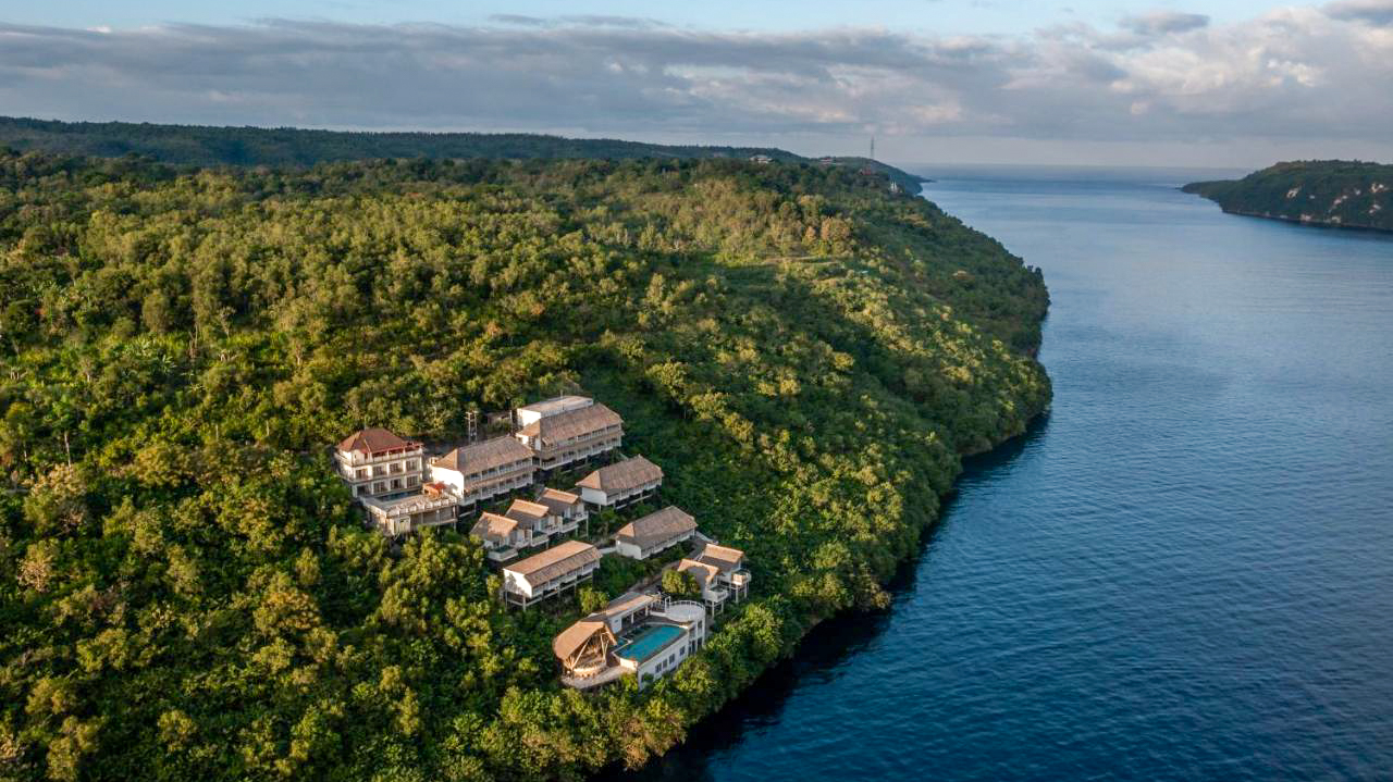 Pramana Natura Nusa Penida resort buildings nestled on a lush green cliff overlooking the blue ocean.