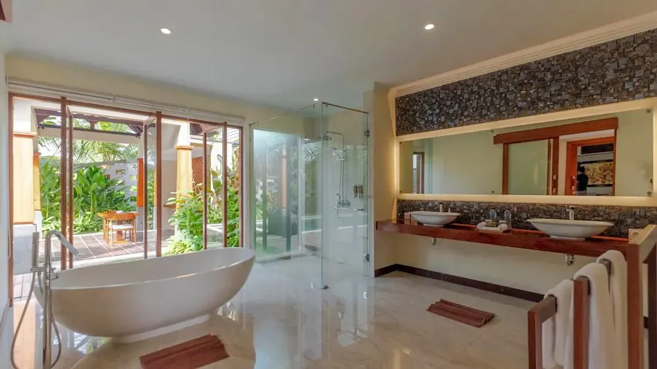 Elegant resort bathroom featuring a freestanding tub, glass shower, double vanity, and lush garden view.