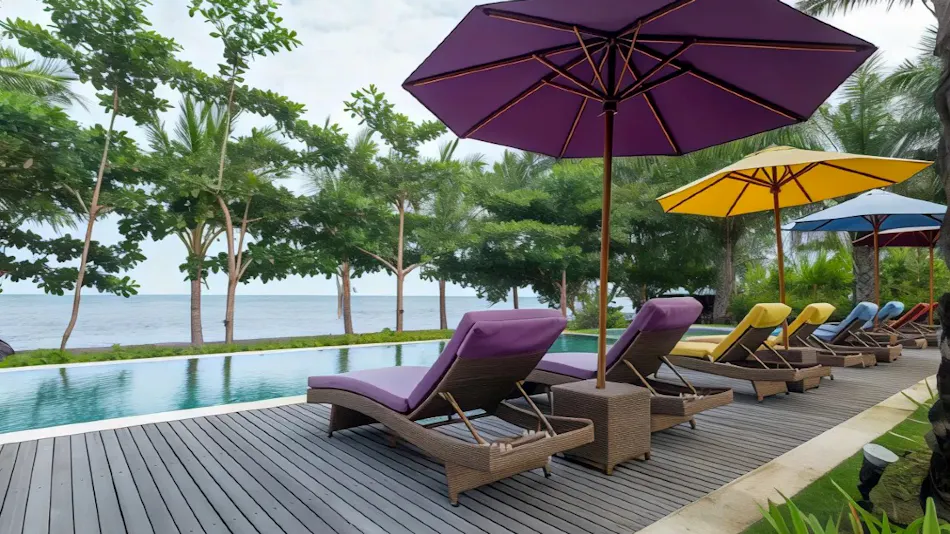 Empty lounge chairs and colorful umbrellas line a resort pool deck overlooking the ocean.