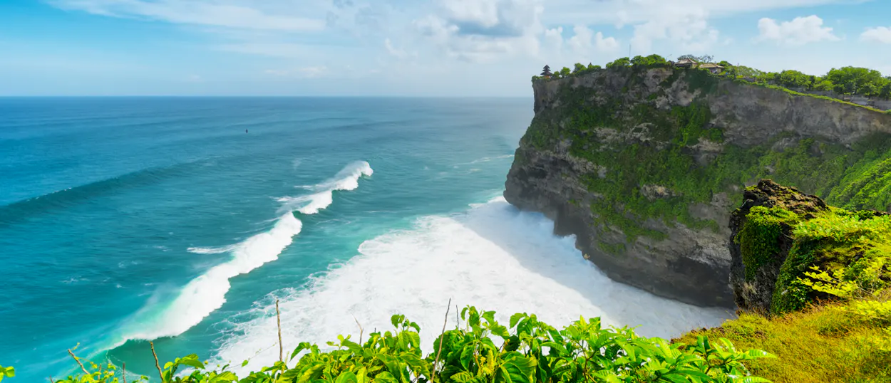 Dramatic clifftop view of the turquoise ocean with crashing waves at Uluwatu Temple, Bali.