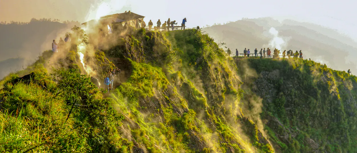 Tourists gather on a misty, lush green ridge at sunrise in Ubud, Bali.