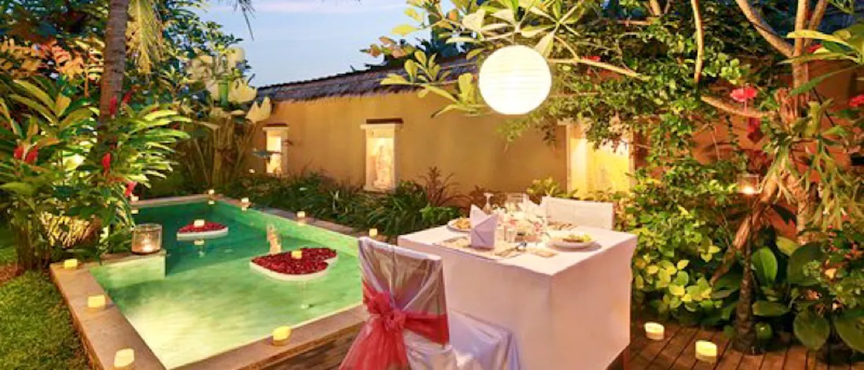 Romantic candlelit dinner setup by a private pool with floating rose petals and lush greenery in Bali.
