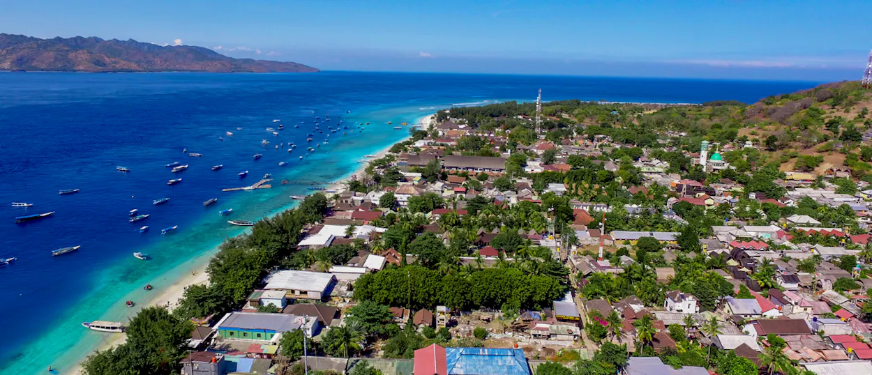Aerial view of Gili Trawangan island, with a white sand beach, turquoise ocean, and many boats.