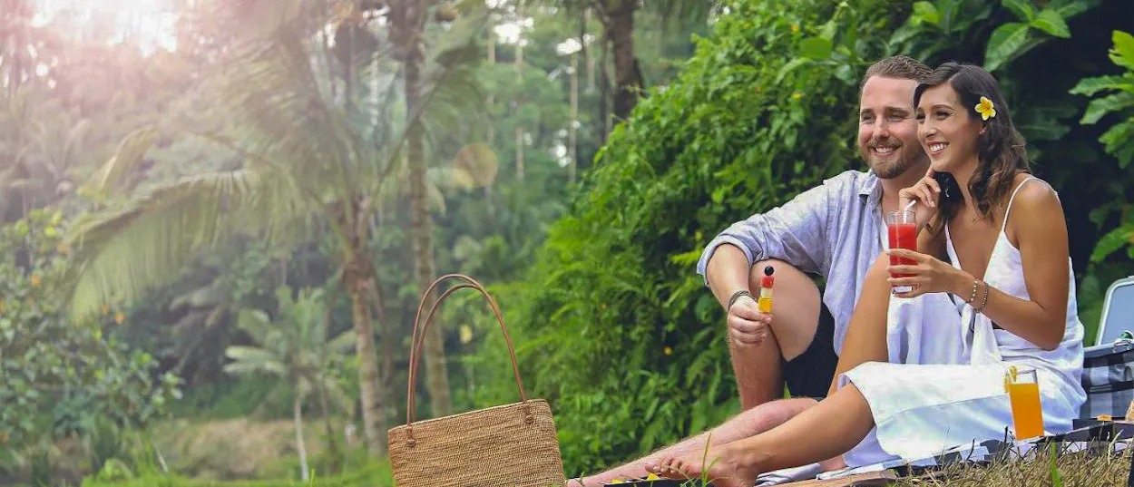 Smiling couple enjoying refreshing drinks on a sunny day in the lush Ubud jungle.