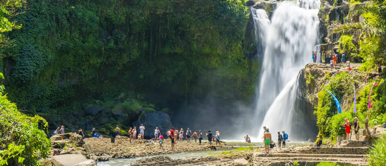 Visitors admire the impressive Tegenungan Waterfall in Ubud, Bali, with lush tropical foliage.