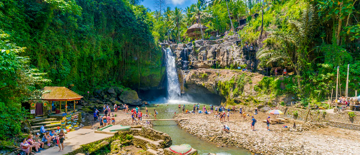 Tourists swim and relax at the beautiful Tegenungan Waterfall surrounded by lush jungle in Bali.