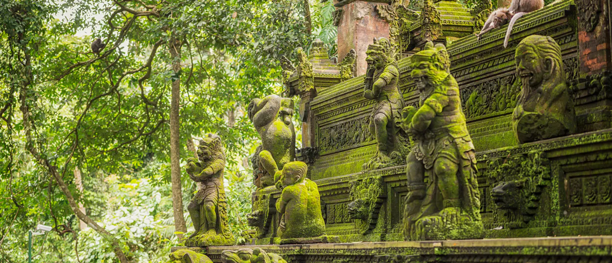 Ancient moss-covered statues and curious monkeys in the lush Sacred Monkey Forest Sanctuary, Ubud.