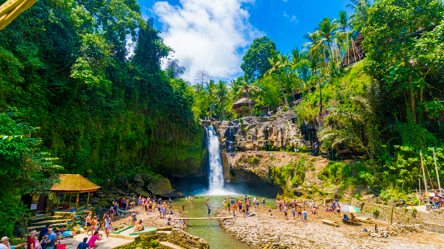 Tourists swim and relax in the pool below Tegenungan Waterfall, surrounded by vibrant green jungle.