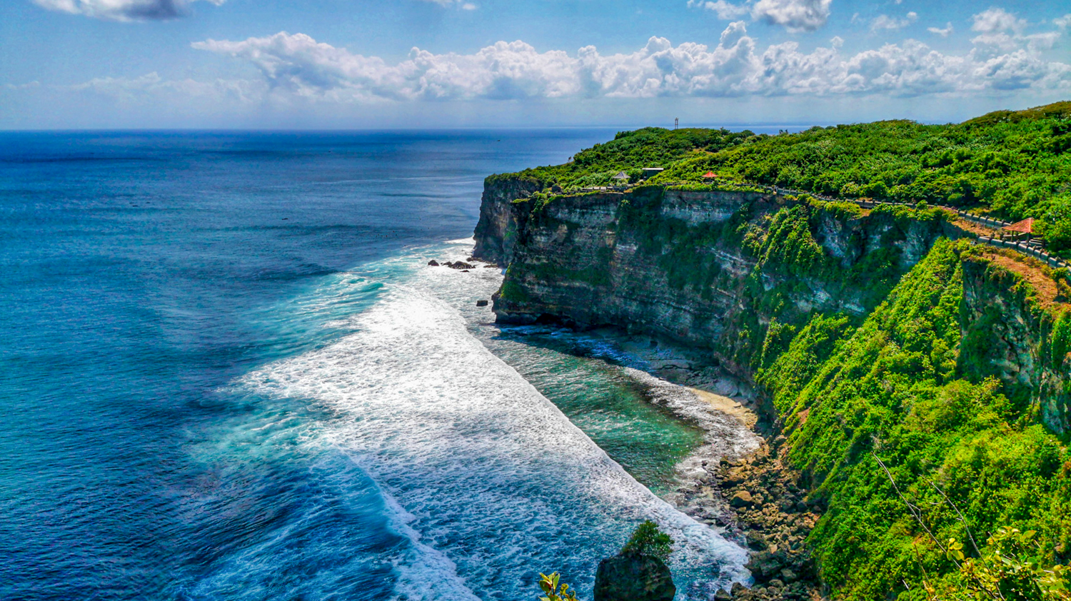 Dramatic Uluwatu cliffs covered in lush greenery rise above the crashing blue ocean waves in Bali.