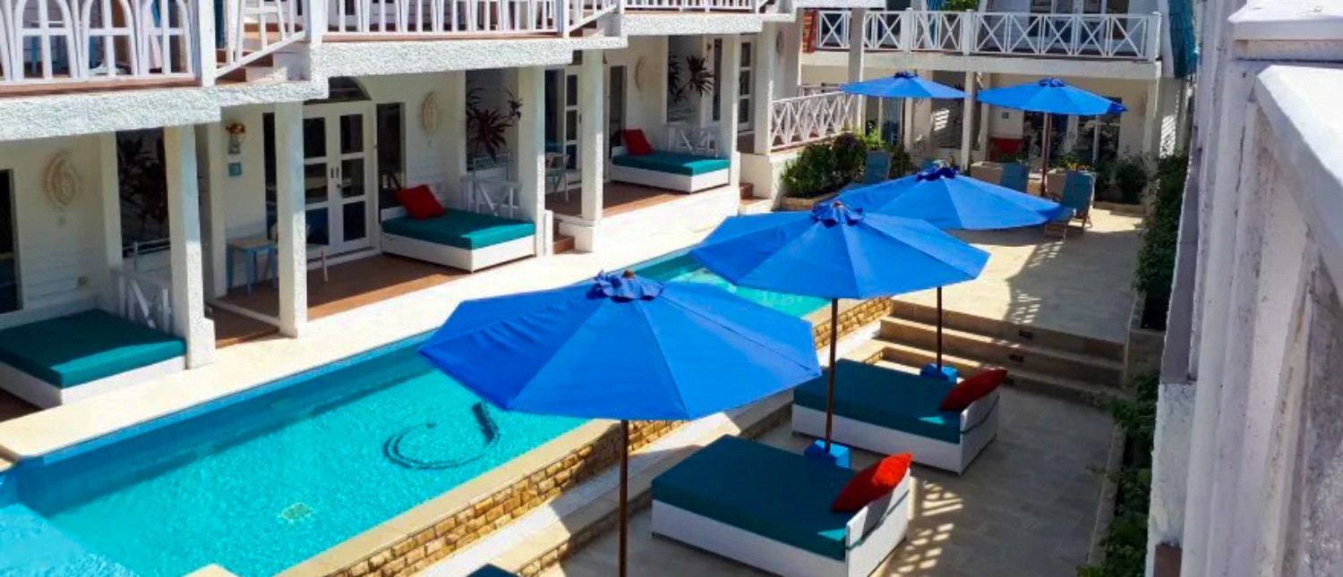 A luxurious Gili Trawangan resort courtyard featuring a swimming pool, blue umbrellas, and comfortable daybeds.