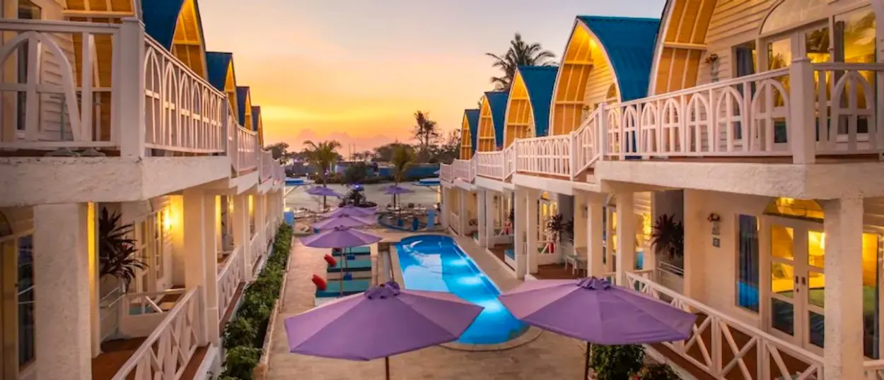 A serene Gili Trawangan resort with white buildings, a swimming pool, and purple umbrellas at sunset.