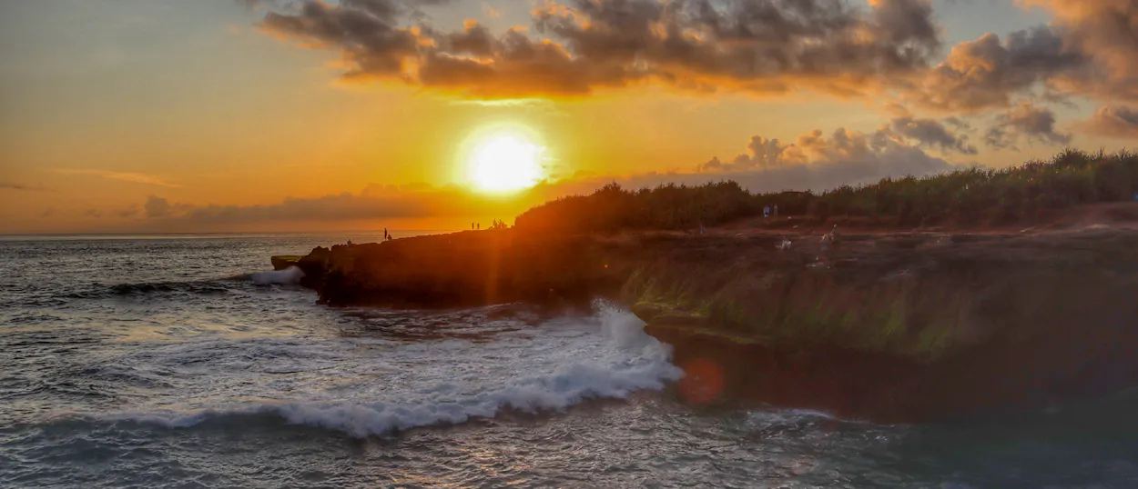 Golden sunset over crashing waves at Devil's Tear, Nusa Lembongan, creating a dramatic evening scene.
