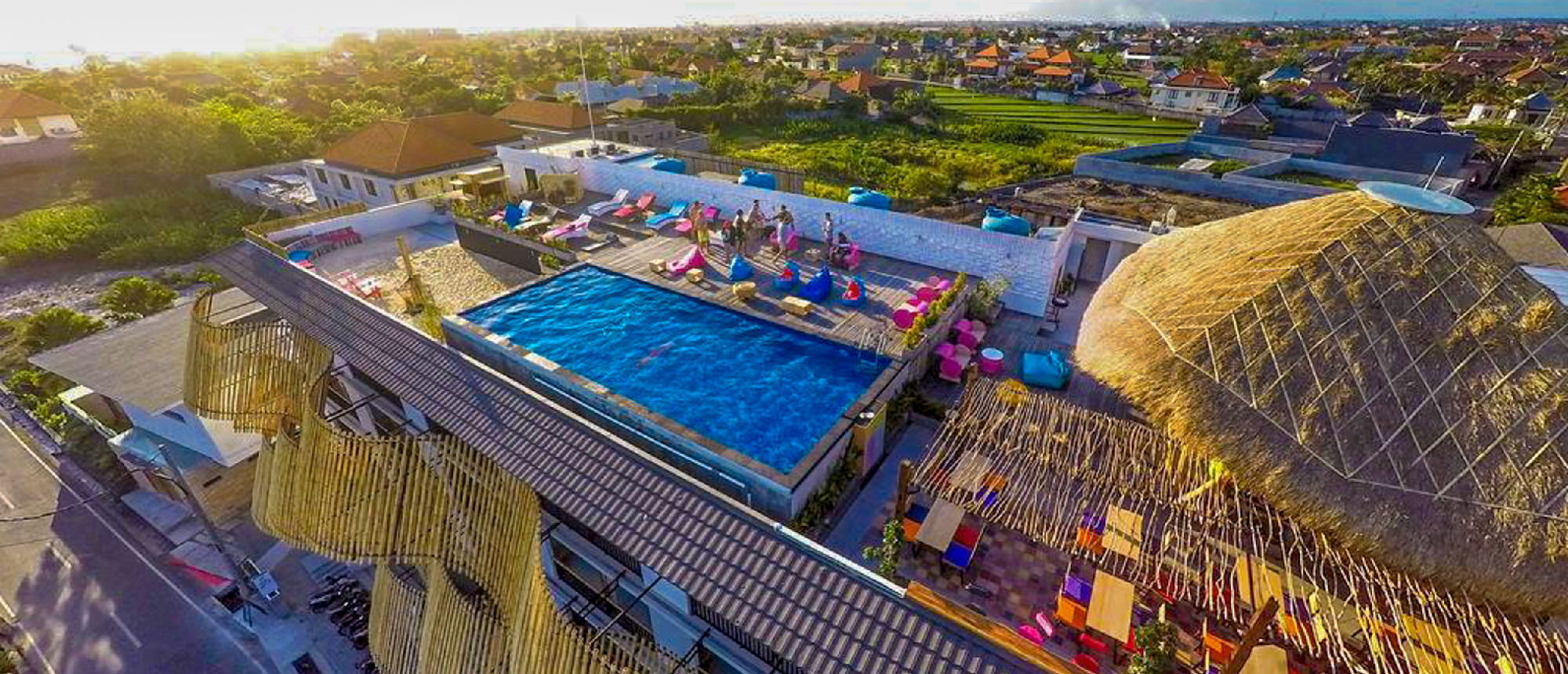 Vibrant rooftop pool and lounge area in Canggu, Bali, with guests relaxing under a warm sunset.