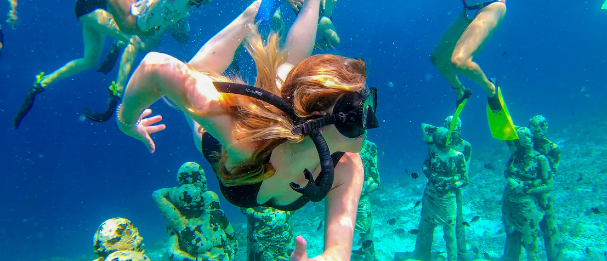 A woman snorkels among the famous underwater statues at Gili Trawangan, enjoying island bliss.