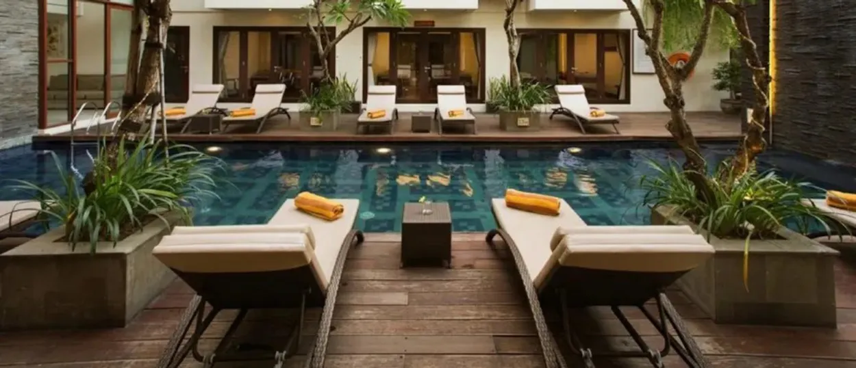 Serene hotel swimming pool in Seminyak, Bali, surrounded by lounge chairs and lush greenery.