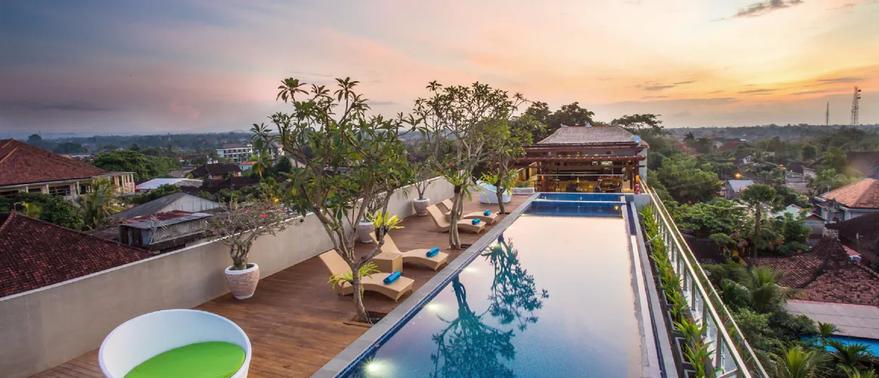 Tranquil rooftop infinity pool with a sunset view of Ubud's lush landscape and traditional buildings.