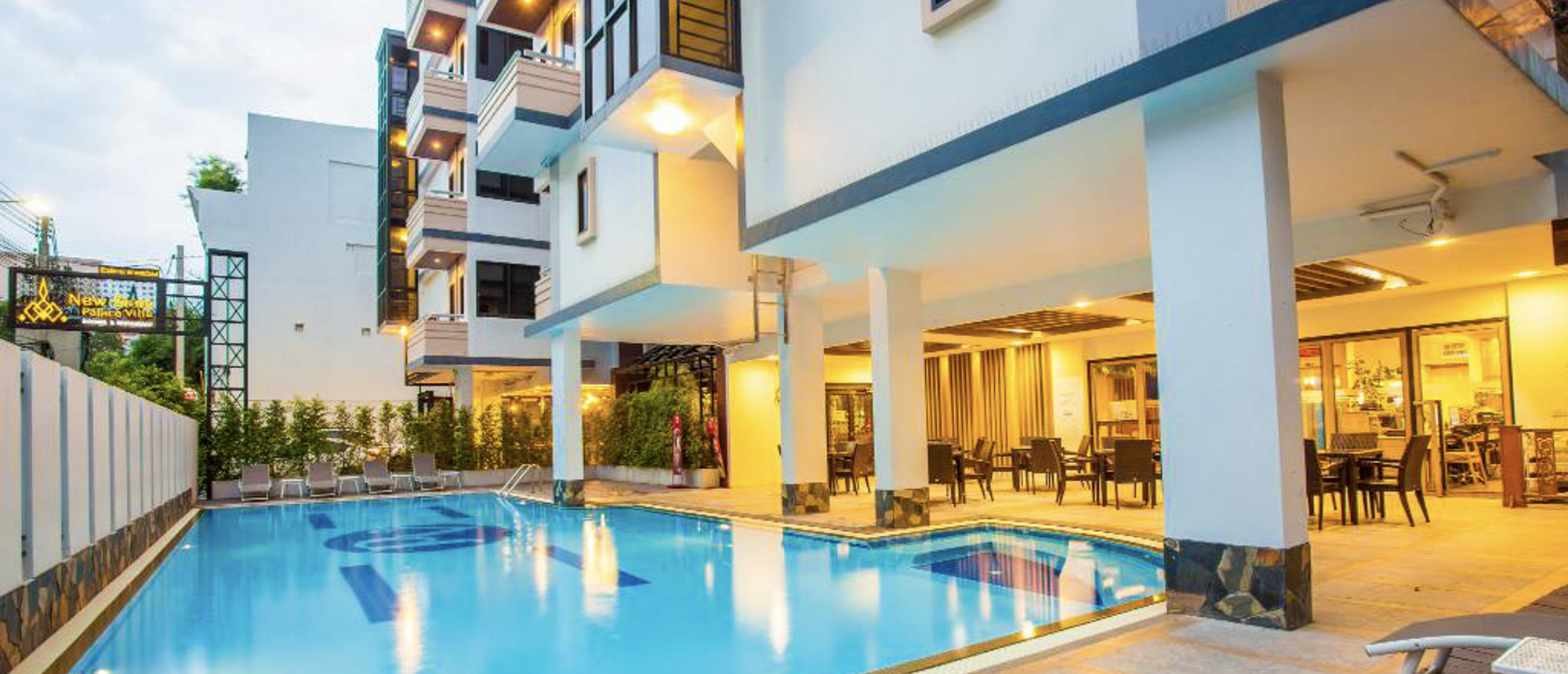An inviting hotel swimming pool and outdoor lounge area in Bangkok, illuminated by warm evening lights.