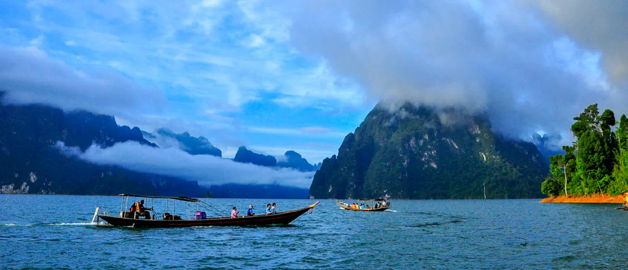 Longtail boats glide across the water among mist-shrouded mountains in Thailand's Khao Sok National Park.