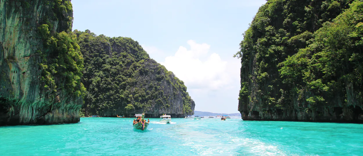 A longtail boat navigates stunning turquoise waters between towering limestone cliffs in Phi Phi Islands.