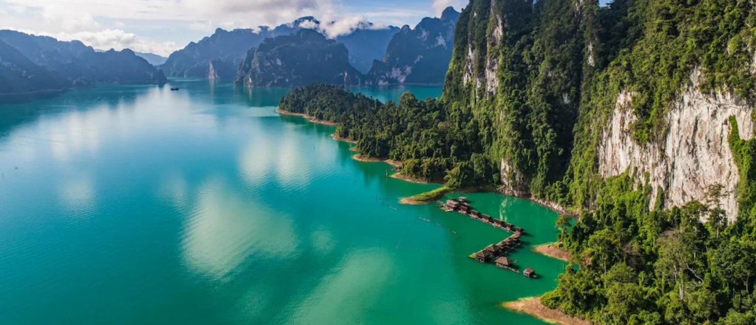 Floating bungalows on turquoise water surrounded by towering limestone karsts and lush jungle in Khao Sok.