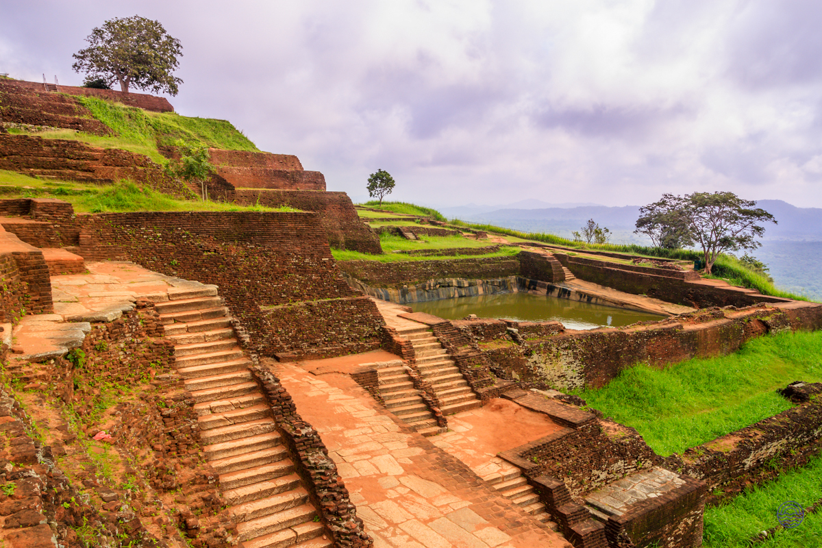 Expansive ancient brick ruins and terraced gardens of Sigiriya Lion Rock under a dramatic cloudy sky.
