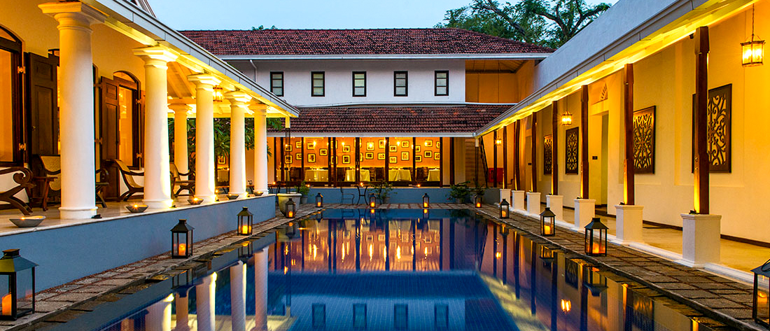Elegant colonial-style hotel courtyard in Colombo with a swimming pool, glowing warmly with evening lights.