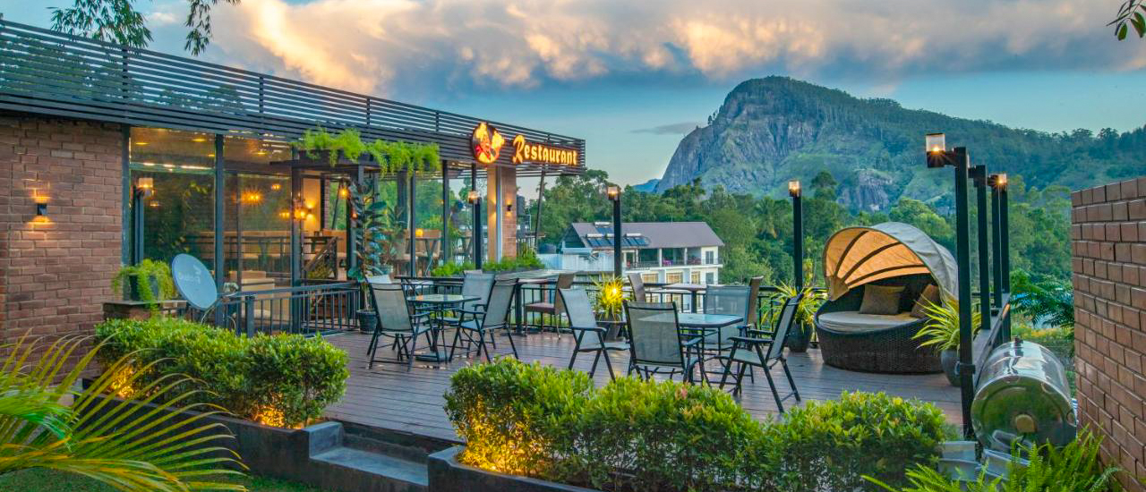 A modern outdoor terrace with dining tables and a lounge overlooking Ella Rock.