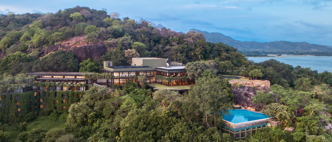 Luxurious hotel and infinity pool nestled in lush green hills overlooking a lake in Sri Lanka.