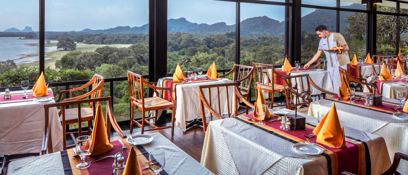 Waiter preparing tables in a beautiful restaurant at Heritance Kandalama with panoramic lake and mountain views.