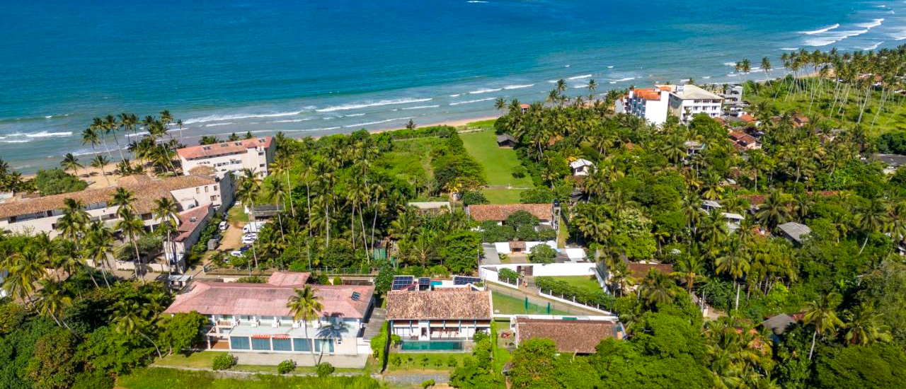 Beautiful aerial view of Weligama's tropical coast, with resorts, palm trees, and the sparkling blue sea.