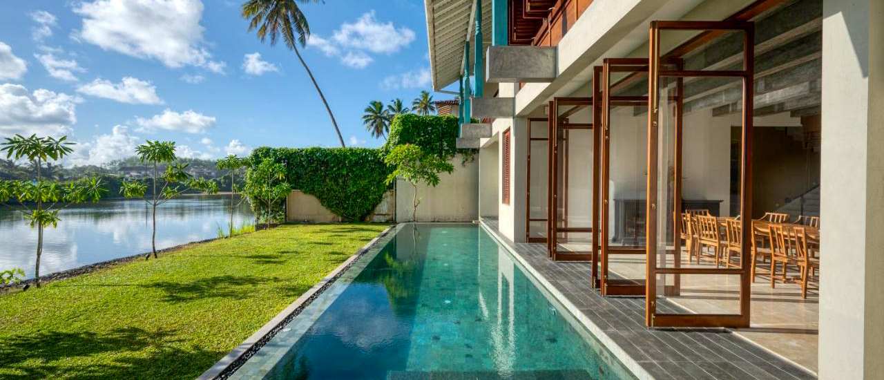 Luxurious villa with a long pool, green lawn, and tranquil lake in Weligama, Sri Lanka.