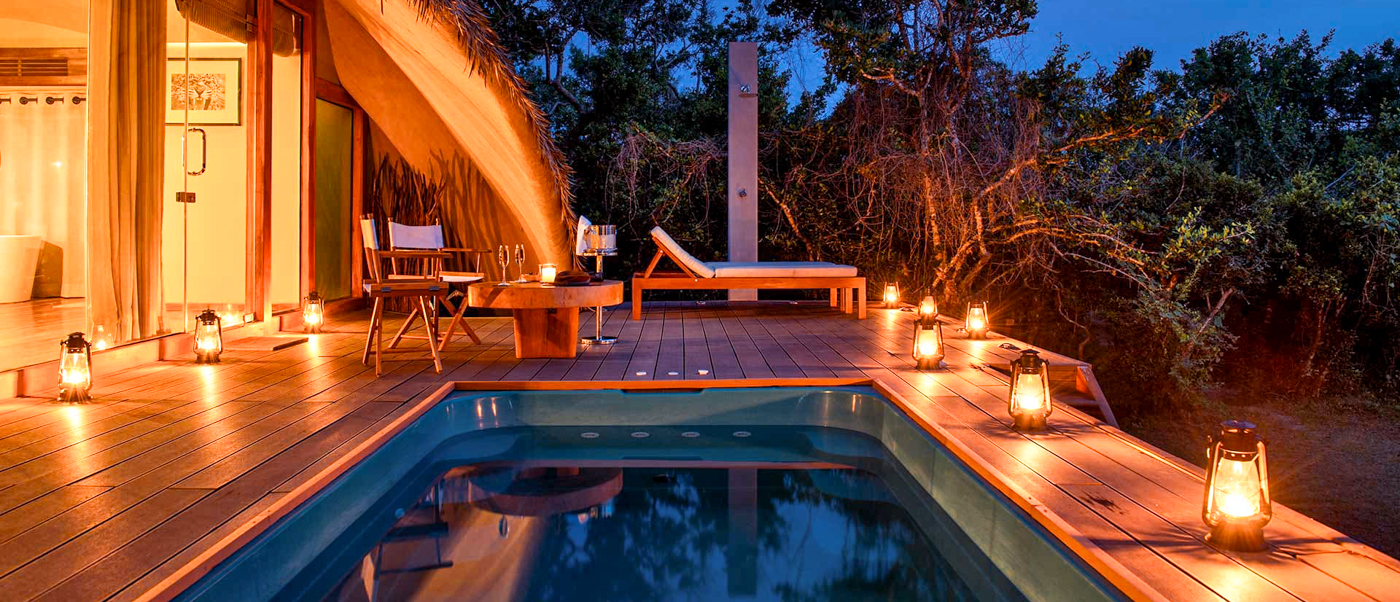 A luxurious private plunge pool and deck lit by lanterns at a wilderness cabin in Yala National Park.