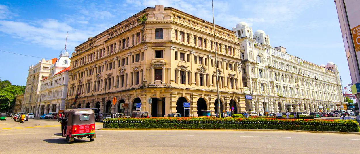 Ornate colonial-era buildings and a red tuk-tuk under a bright blue sky in Colombo.