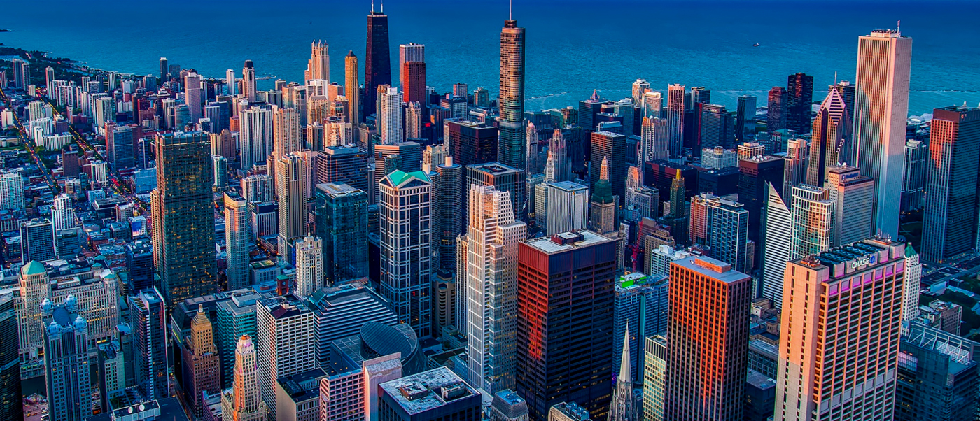 Dense cityscape with many skyscrapers reflecting warm light against a clear blue sky.